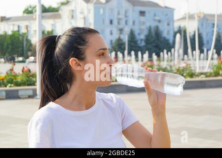 Joven mujer deportiva bebiendo agua fresca de la botella en la ciudad que se refresca. Foto de stock
