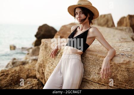presión estrés fascismo Retrato de mujer en bralette negro y pantalón blanco apoyado sobre roca en  la playa Fotografía de stock - Alamy