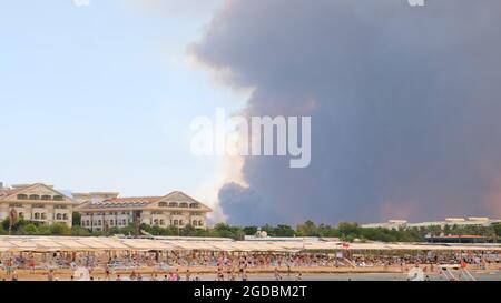 Humo de los incendios forestales que se elevan sobre una playa en Antalya, Manavgat ciudad turística de Turquía. Vista con la gente en la playa: Antalya, Manavgat Turquía - julio Foto de stock