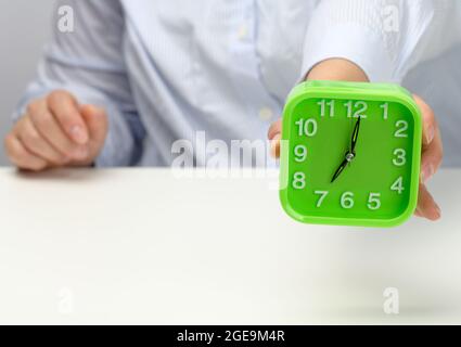 la mano de la mujer sostiene un reloj cuadrado verde el reloj