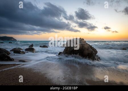 Una puesta de sol en la playa con la ola retrocediendo en la playa. Foto de stock