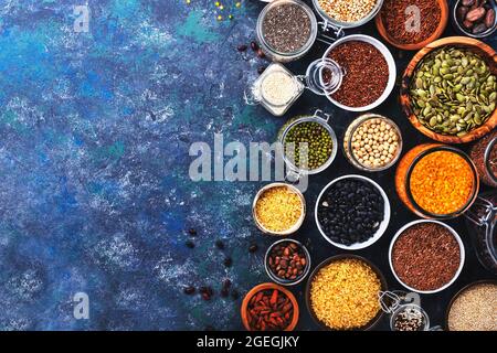 Juego de superalimentos, legumbres, cereales, nueces, semillas en cuencos sobre mesa azul. Espacio de copia, vista superior Foto de stock