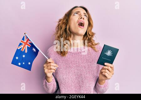 Una joven caucásica con bandera australiana y pasaporte enojada y loca gritando frustrada y furiosa, gritando con ira mirando hacia arriba. Foto de stock