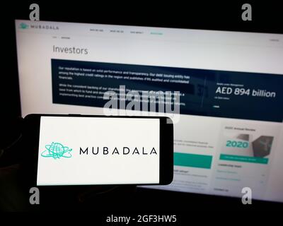 Persona que sostiene el teléfono móvil con el logotipo del inversor de Emirati Mubadala Investment Company PJSC en la pantalla delante de la página web. Enfoque en la pantalla del teléfono. Foto de stock