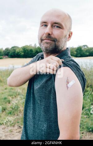 Hombre vacunado mostrando vendaje por tatuaje en el brazo Foto de stock