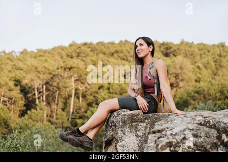 Caminadora femenina con mochila sentada sobre roca