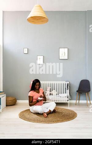 Mujer embarazada sosteniendo bebés mientras estaba sentada en la alfombra en casa Foto de stock