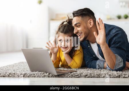 Feliz Padre de Medio Oriente y Niño femenino haciendo videollamada con ordenador portátil en casa