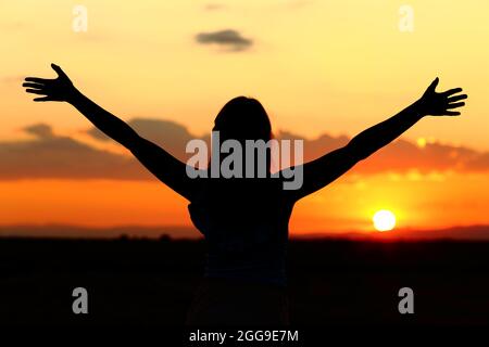 Vista posterior retrato de una silueta de mujer que celebra los brazos estirados al atardecer