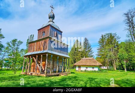 El alto campanario de madera de la iglesia de intercesión con pequeño porche, escalera y la casa del sacerdote blanco en el fondo, Pereiaslav Scansen, Ucrania Foto de stock
