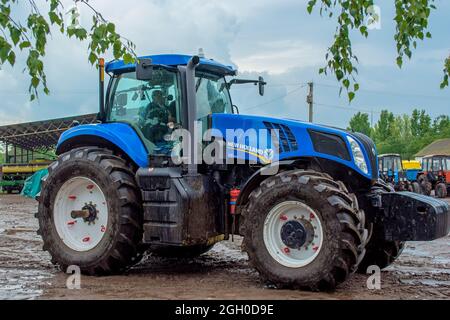 Cherkasy, Ucrania - 02 de junio de 2015:Potente tractor azul New Holland montando en el barro bajo la lluvia.