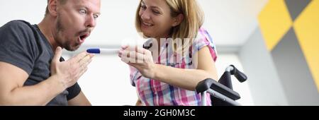 Una mujer alegre en silla de ruedas muestra una prueba de embarazo de hombre sorprendido