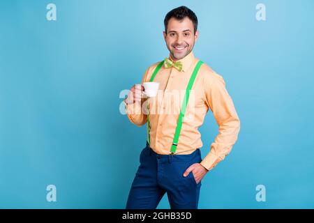 Foto de alegre chico sostener taza beber café ropa verde tirantes camisa  lazo corbata aislado color azul fondo Fotografía de stock - Alamy