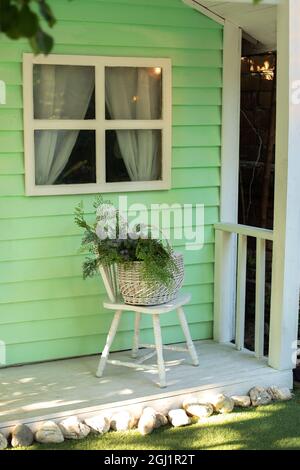 Acogedora terraza con silla y cesta con flores. Decoración en el patio de verano para relajarse. Elegante decoración otoñal en el porche de la casa.