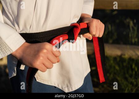 sujetando en un cinturón negro su uniforme de taekwondo antes de entrenar al aire libre Fotografía de stock -