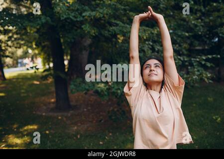 Sport Milennial Indian Girl in Casual Ropa Estirarse antes de entrenar en el parque, haciendo ejercicios de calentamiento. Foto de stock