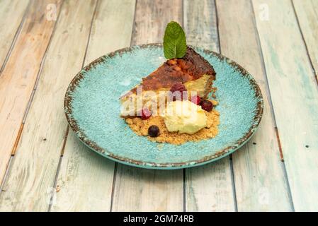 Maravillosa rebanada de tarta de queso con galletas, bayas y helado de vainilla en un plato azul Foto de stock
