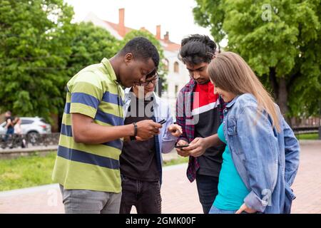Estudiantes universitarios multiétnicos que comprueban la información mediante teléfonos móviles Foto de stock