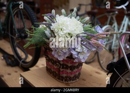 Ramo de hortensias y altramuces artificiales blancos y azules en una cesta de mimbre en una ventana de la tienda Foto de stock