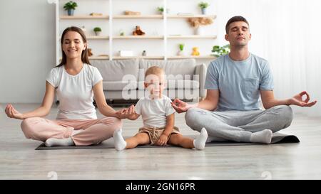 Familia feliz de tres con el bebé pequeño meditando juntos en el hogar Foto de stock