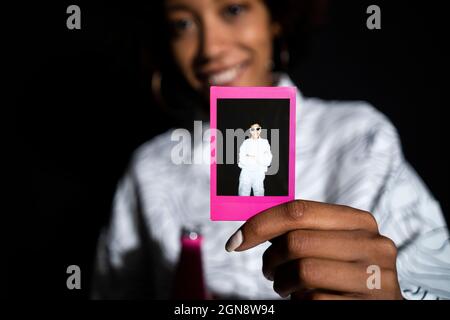 Mujer que muestra una fotografía polaroide contra fondo negro
