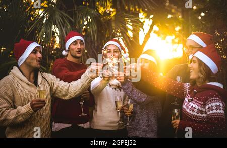 Grupo de amigos con sombreros de santa celebrando la Navidad con champán vino brindis al aire libre - Concepto de vacaciones tropicales con jóvenes disfrutando del tiempo Foto de stock