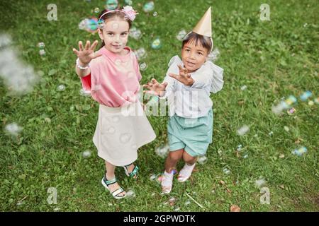 Retrato en ángulo de dos niñas jugando con burbujas mientras disfruta de la fiesta de cumpleaños al aire libre en verano
