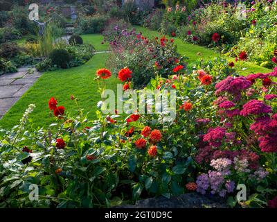 Chenies Manor Jardín hundido a finales de septiembre. Césped alrededor del estanque ornamental, vibrante fronteras dahlia bellamente abastecido. Foto de stock