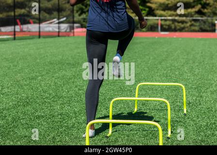 Una niña de la escuela secundaria está realizando ejercicios de velocidad y agilidad sobre obstáculos sin zapatos.
