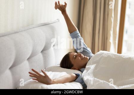 Chica feliz despertando en ropa de cama blanca, estirando los brazos
