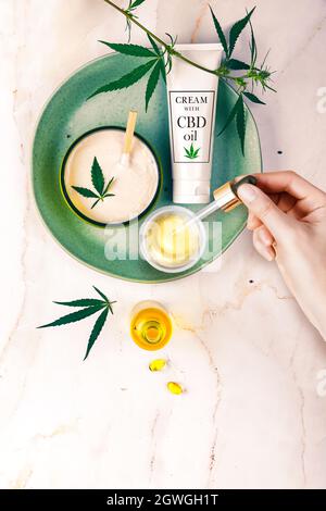 Pipetear con aceite cosmético CBD en manos femeninas con cosméticos, crema con hojas de cannabis y cáñamo