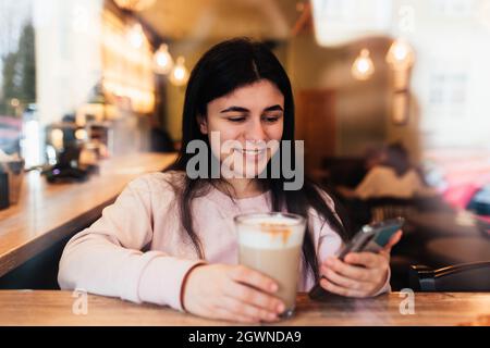Chica Smiling, bebidas Café en Café y teléfono de lectura. Fondo borroso. Foto de alta calidad