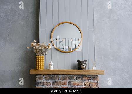 Interior minimalista escandinavo con estilo. Interior moderno de una casa de campo en colores gris y amarillo. Espejo redondo sobre la chimenea de ladrillo en el Foto de stock