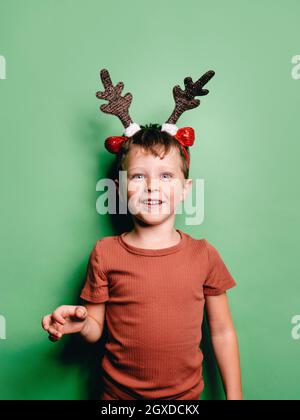 Chico sonriente con de reno diadema de pie sobre fondo verde y mirando la cámara Fotografía de stock - Alamy