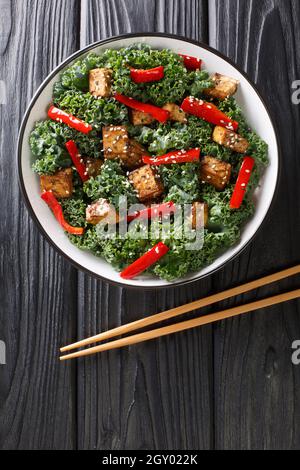 Ensalada de dieta hecha de tofu frito, pimientos, col rizada y semillas de sésamo en un bol sobre la mesa. Vista vertical superior desde arriba Foto de stock