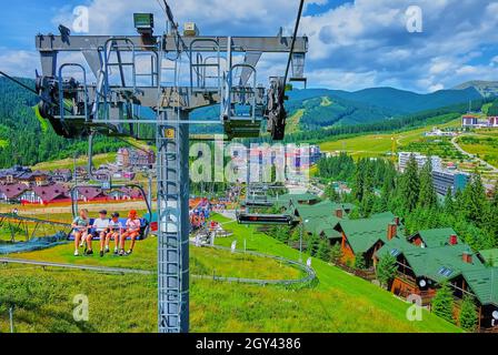 BUKOVEL, UCRANIA - 25 DE JULIO de 2021: El telesilla, a lo largo de la verde pendiente del Monte Bukovel con atracciones turísticas, casas de campo, senderos y alta spruc Foto de stock