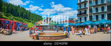 BUKOVEL, UCRANIA - 25 DE JULIO de 2021: Panorama de la pequeña y concurrida plaza con hotel turístico, cafés al aire libre, tiendas y la fuente en medio de la zona peatonal Foto de stock