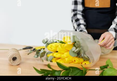 La mujer de la florería hace un ramo de tulipanes amarillos frescos. Entrega de flores Foto de stock