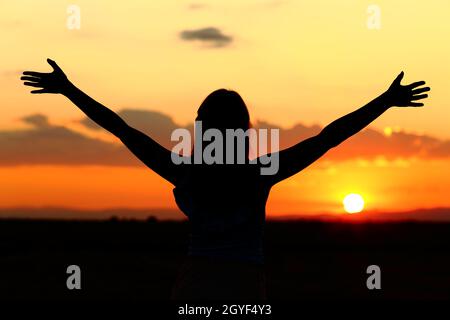 Vista posterior retrato de una silueta de mujer que celebra los brazos estirados al atardecer