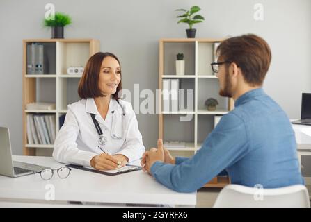 Smiley doctor hablando con su paciente sentado en el escritorio en su oficina, clínica u hospital Foto de stock
