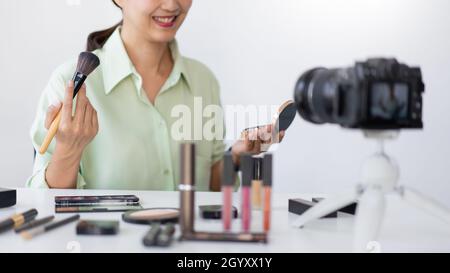 Un influencer de la belleza que aplica la rubor del polvo en su mejilla usando el cepillo del maquillaje delante de una cámara fotográfica. Foto de stock