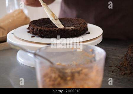 Proceso de elaboración de pasteles. Una mujer impregna trozos de pastel de  chocolate cocido con jarabe de cereza. Receta paso a paso para el pastel de  chocolate. Serie. Conc. De hornear Fotografía