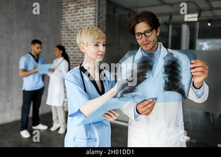 Dos médicos profesionales, hombre y mujer, que examinan la radiografía de los pulmones del paciente, hablan de casos clínicos difíciles mientras se reúnen por la mañana con m. Foto de stock
