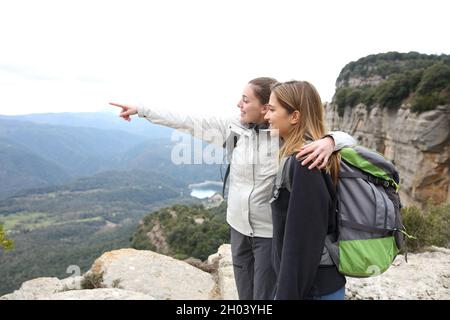 Dos felices excursionistas de pie en la cima de un acantilado apuntando hacia fuera Foto de stock