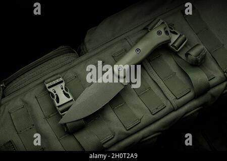 Un cuchillo militar moderno y una funda de plástico para él las armas  afiladas yacen en una mochila militar de color oliva