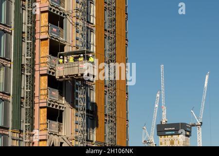Trabajo en altura: Los trabajadores de la construcción en un ascensor llevan el EPI mientras trabajan en un sitio de Glasgow con grúas torre en el fondo. Foto de stock
