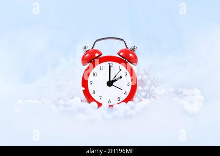 Cambio de hora de invierno para el horario de verano en Europa el 31st de octubre concepto con reloj de alarma rojo entre nieve