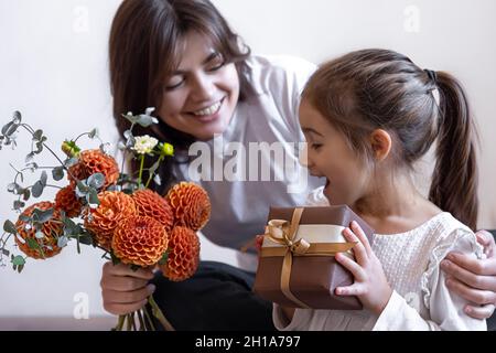 La niña le da a su mamá una caja de regalo y un ramo de flores de