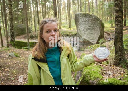 Una mujer geocaching. Las mujeres en los bosques encuentran el contenedor de geocaché cerca de la piedra grande Foto de stock
