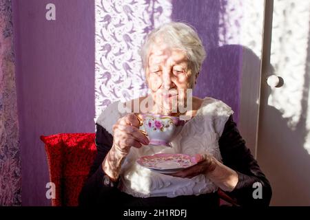 Mujer mayor disfrutando de una taza de té o café en el fondo soleado de su casa Foto de stock